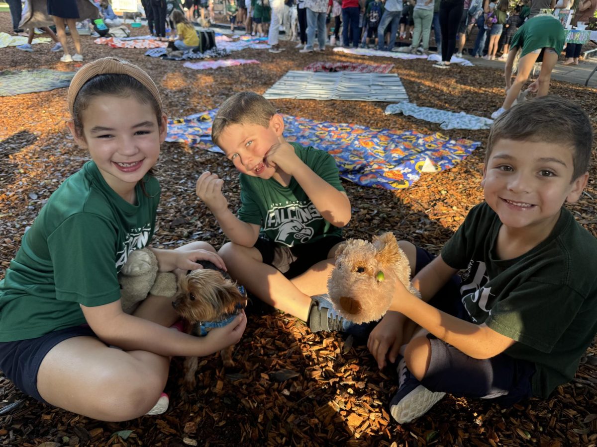 Three friends grin big while celebrating the blessing of their stuffed animals and dog.