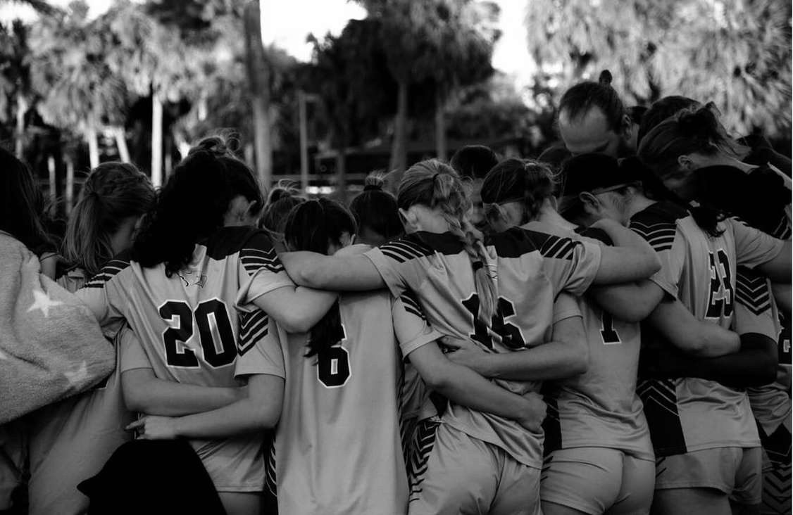 Girls varsity soccer team huddles together for pre game prayer. 