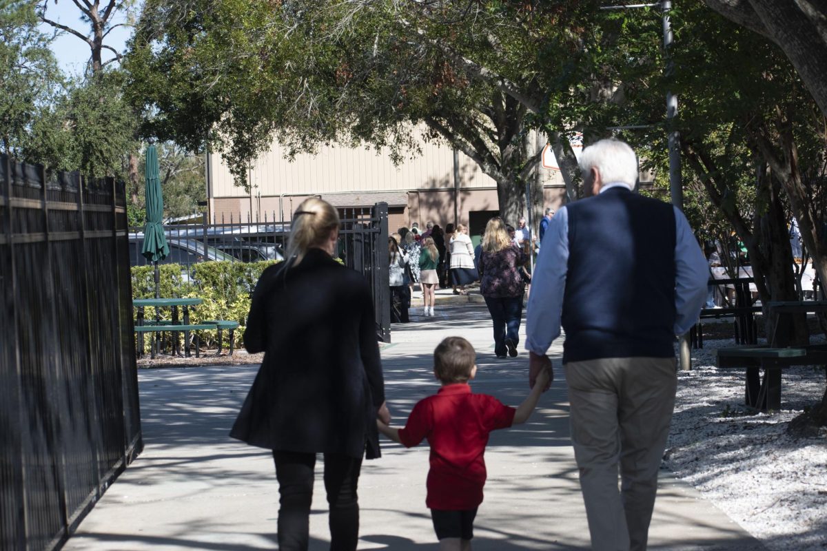 A lower schooler walks hand-in-hand with his grandparents as he escorts them to the gym.